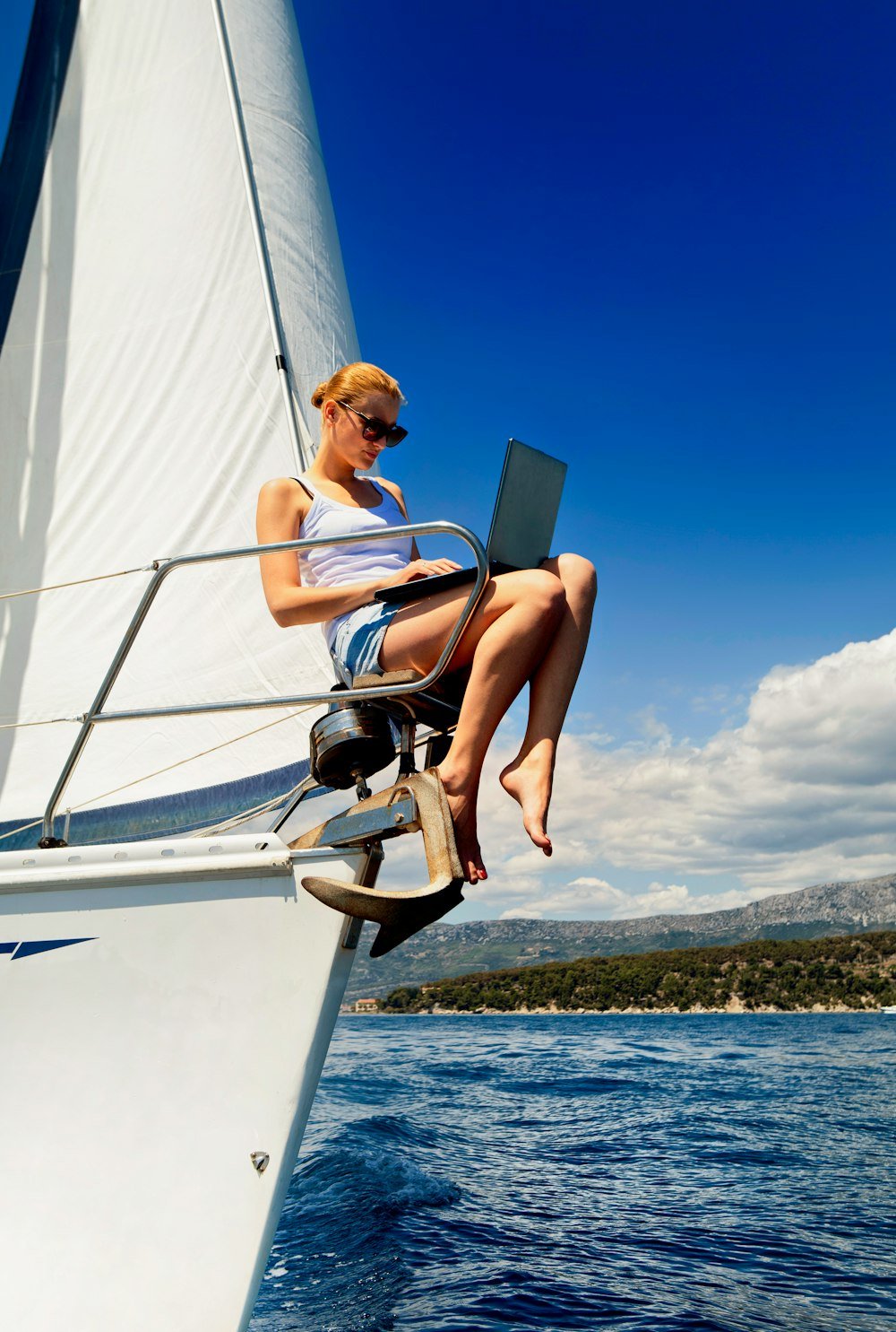 Working on the move. Young woman with laptop computer writing while sailing on the yacht on the ocean.